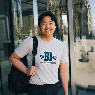 Man posing in front of BI school wearing grey t-shirt with BI logo